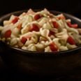 Tazón pequeño de una ensalada cremosa con pimiento rojo, junto a la ensalada César en el pizarrón del menú