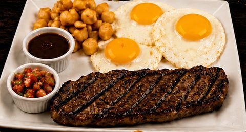 Bistec a la parrilla con tres huevos estrellados, papas de desayuno y salsa